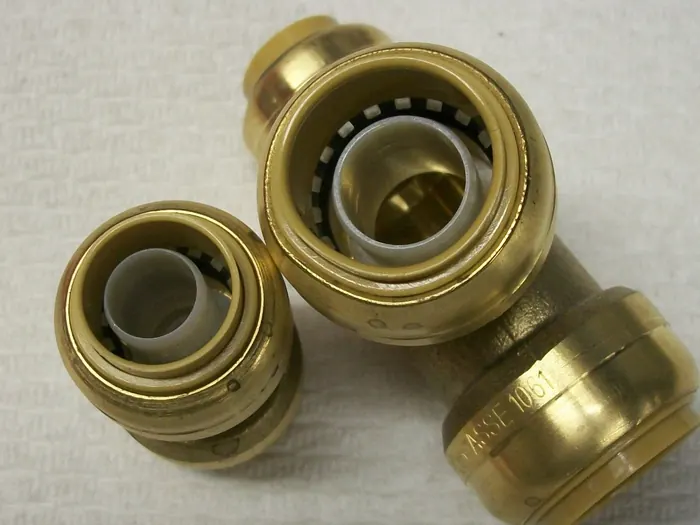 Two brass push-to-connect fittings seen end-on, showing the stainless gripping teeth and plastic liner inside