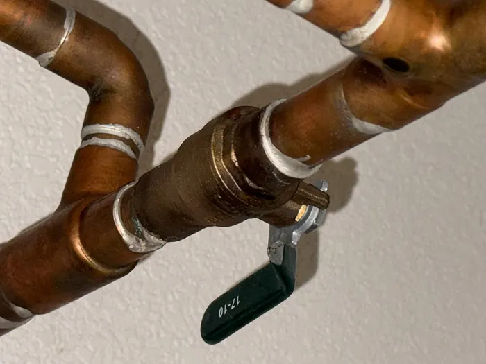 Copper water pipes with soldered elbows and a ball valve with a black lever, running across a wall