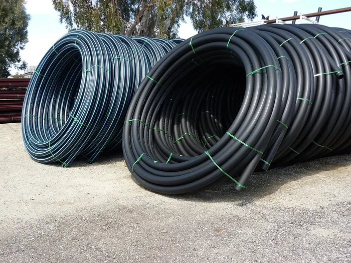 Large coils of black polyethylene water pipe, some with blue stripes, tied with green straps in a yard