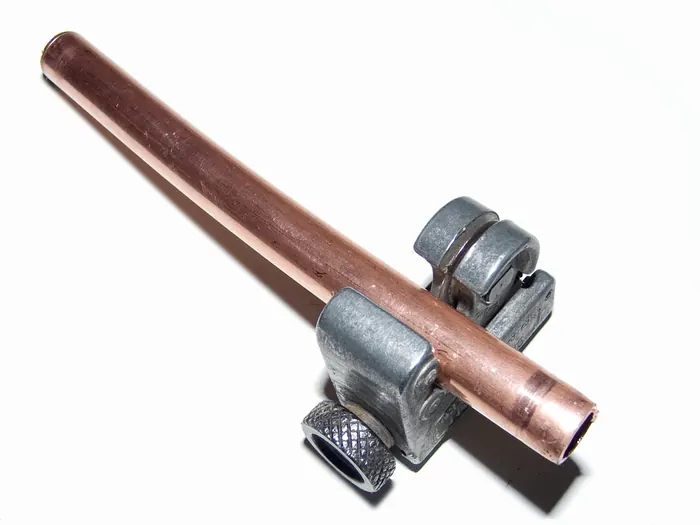A copper tube clamped in a small tubing cutter on a white background